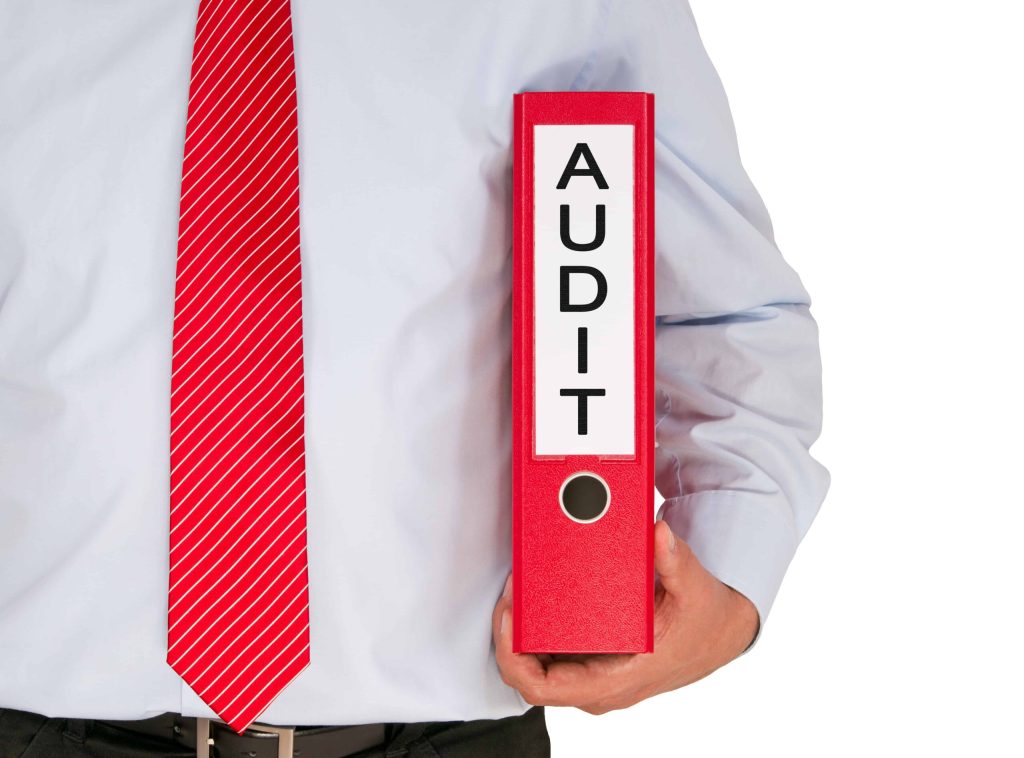 Man in business attire holding a binder that says "audit"