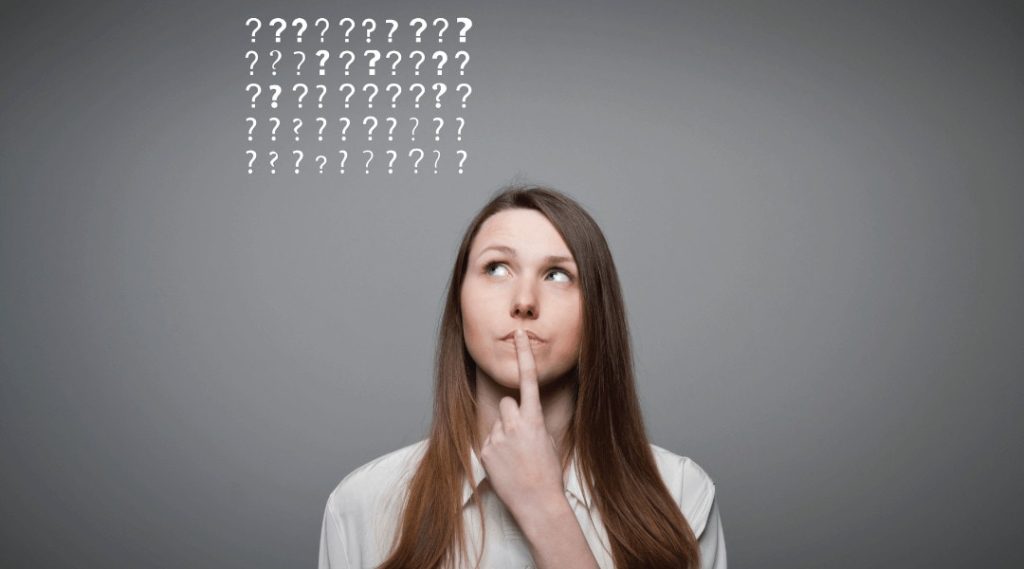 a headshot of a person looking at question marks floating above her head thinking and holding her finger to her lip.