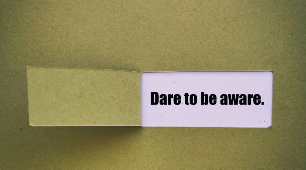 "dare to be aware." printed on pink paper being made visible from a cut out of green paper.